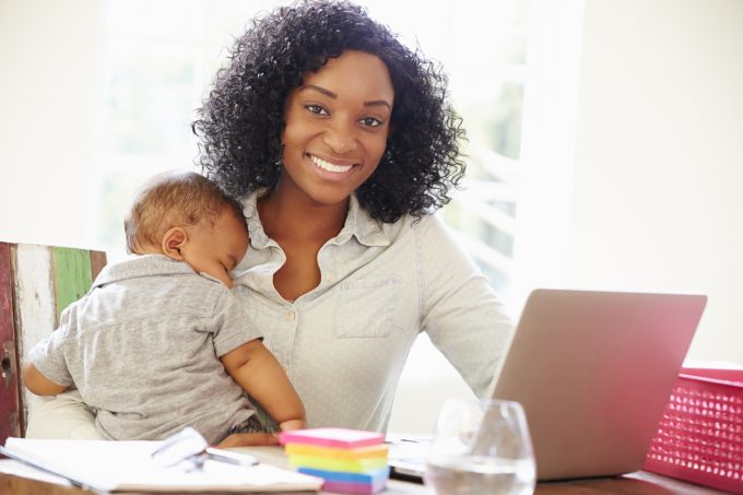 Mother With Baby Working In Office At Home With Laptop Smiling To Camera