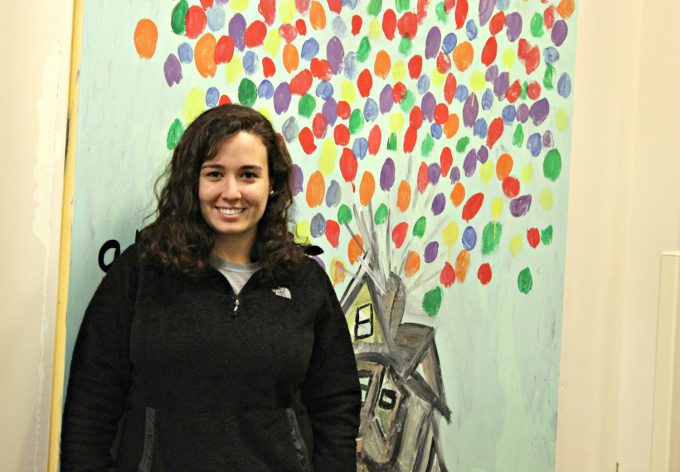 Mental Health Specialist Maria standing in front of artwork done by inpatient mental health patients