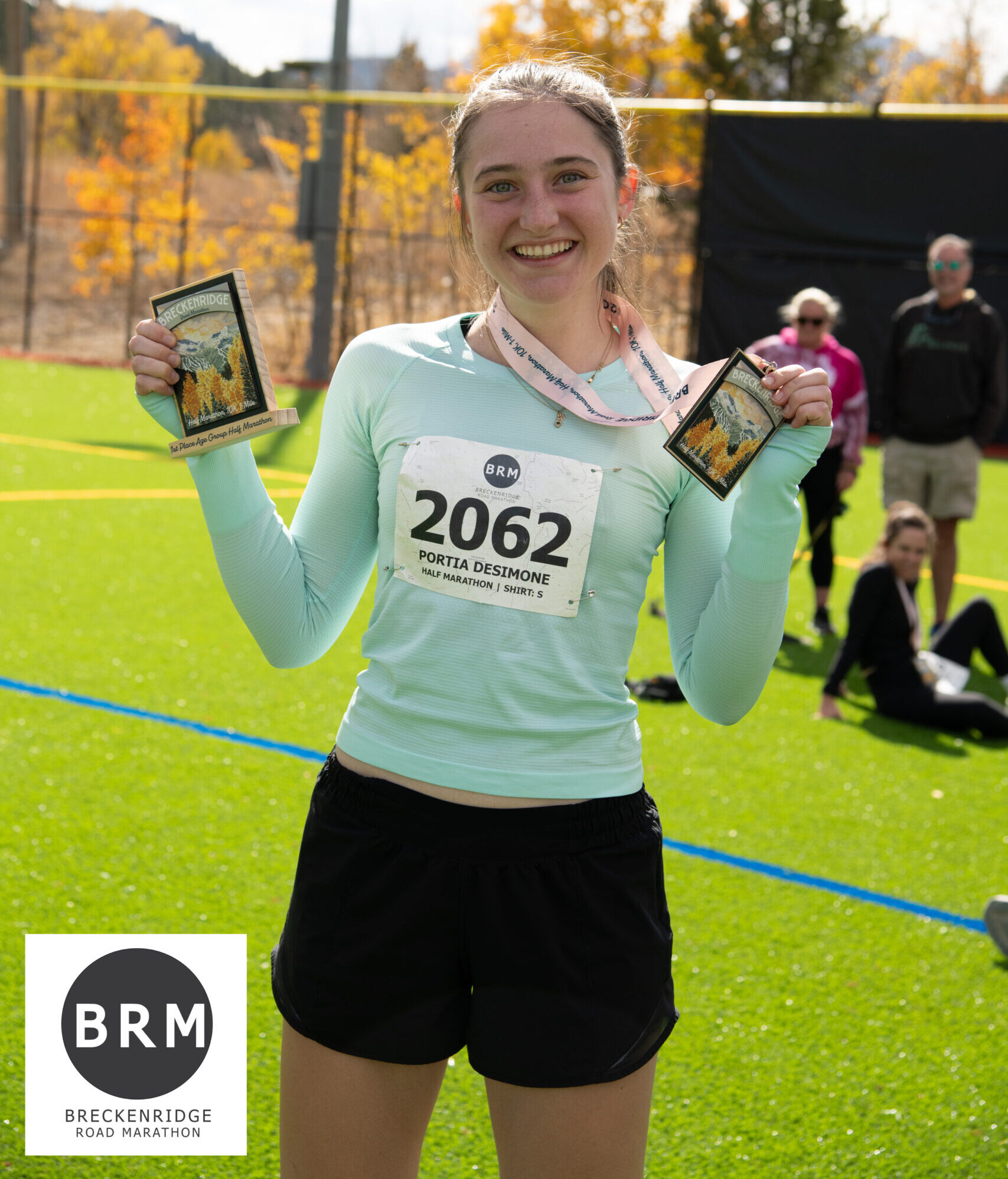 Portia standing on a field holding up a medal she won during the Breckenridge Road Marathon.