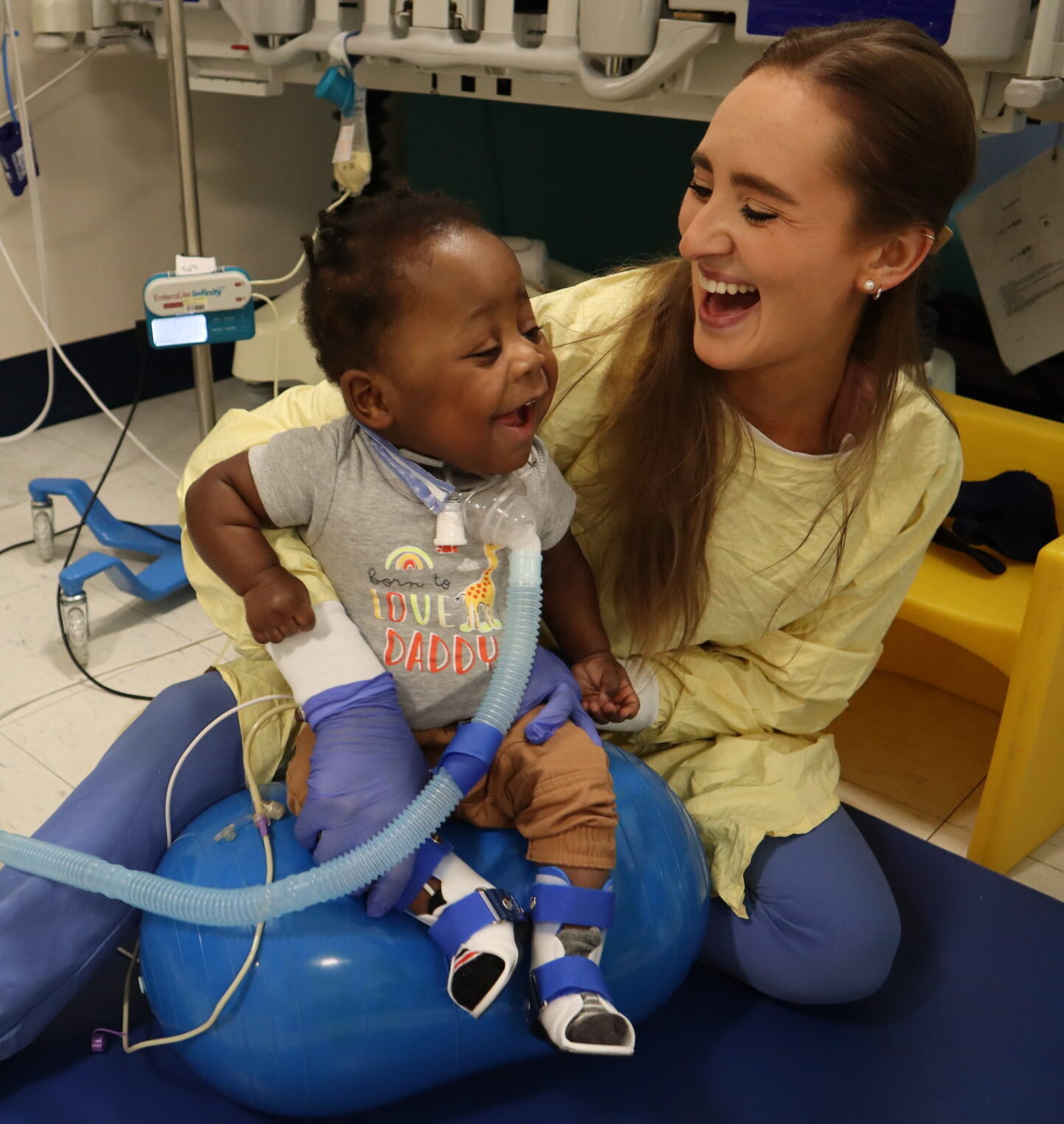 Physical Therapist, Erin Donnelly sits on a mat supporting a child on a ventilator sitting on a squish ball during a physical therapy session at Franciscan Children's.