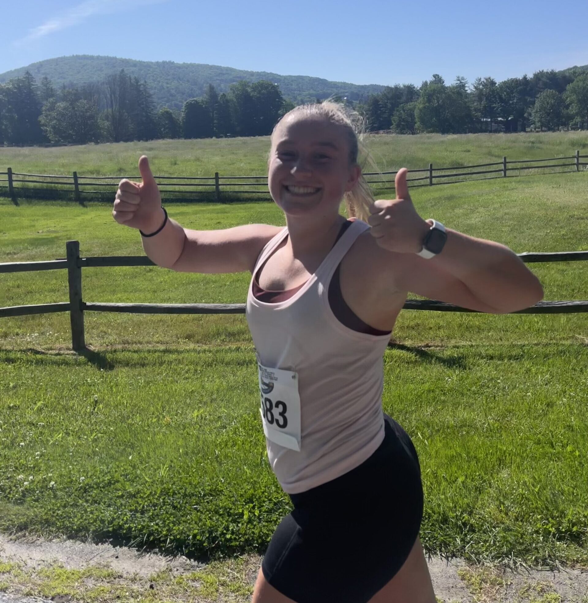 Marie running on a dirt path, smiling and holding two thumbs up.