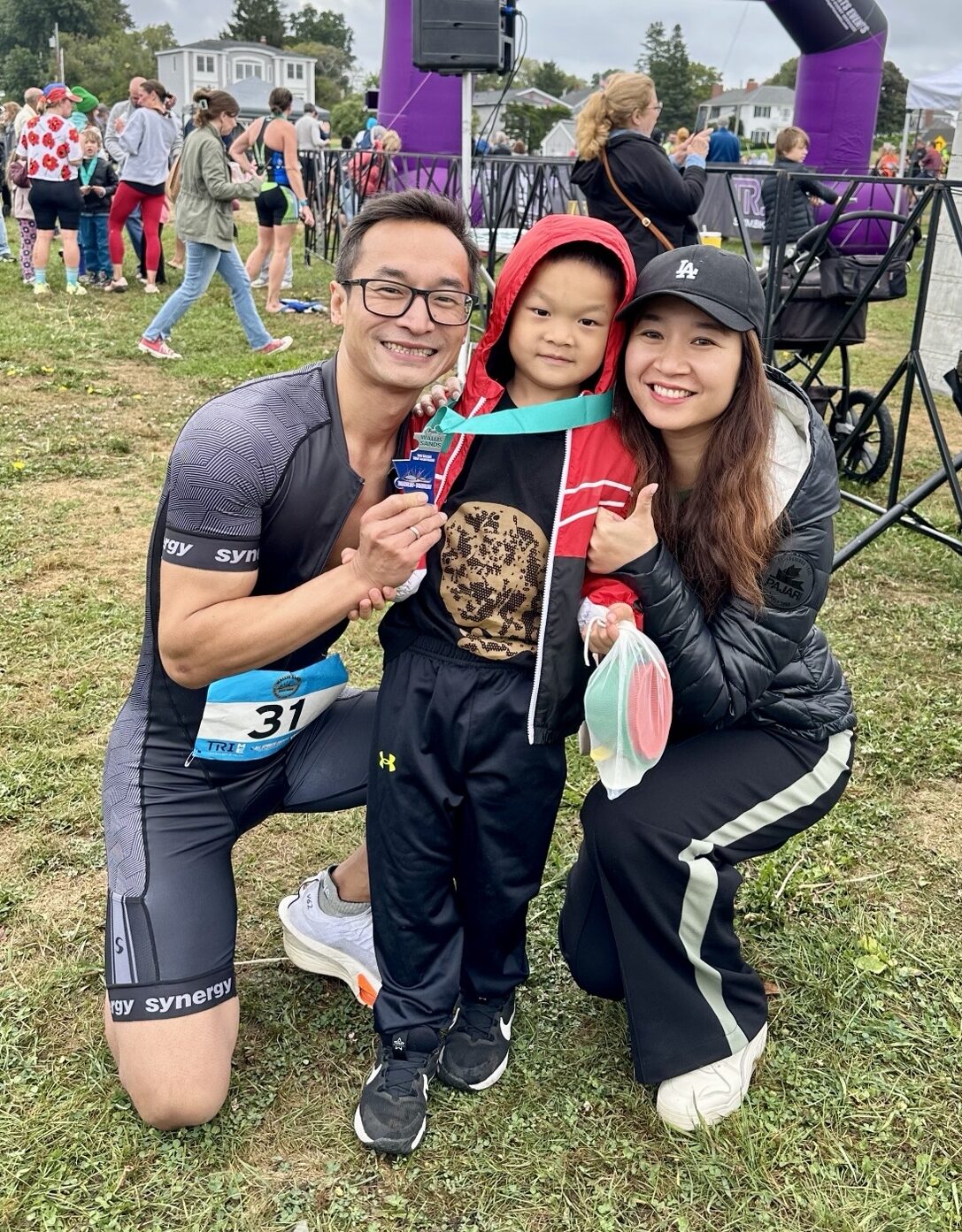 Xian smiles and kneels down next to his young son and wife after finishing a marathon.